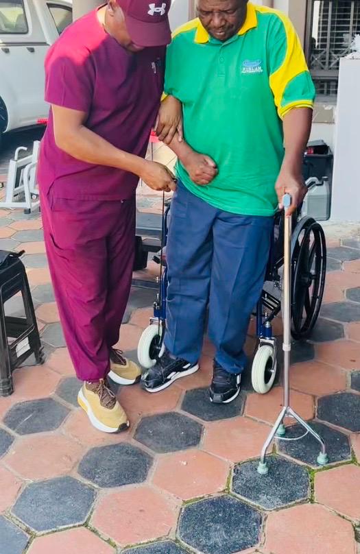 A physiotherapist helping a man stand with a walker during a home-visit session